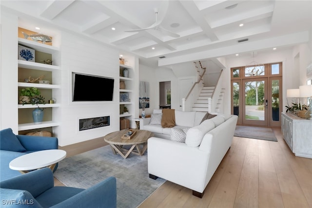 living room with built in features, light wood-type flooring, beam ceiling, coffered ceiling, and ceiling fan