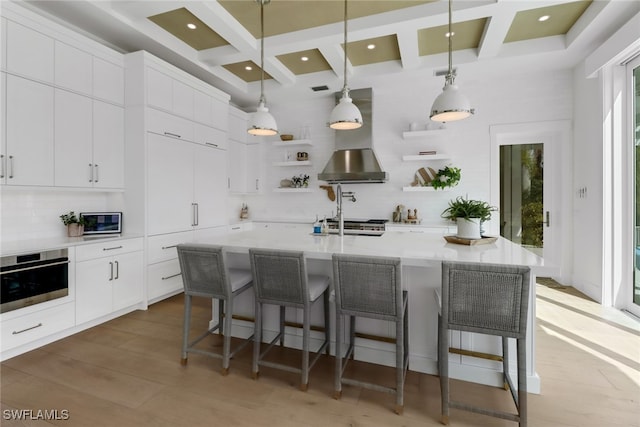 kitchen with a center island with sink, pendant lighting, a breakfast bar area, oven, and white cabinetry