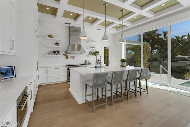 kitchen featuring sink, high end stove, white cabinets, wall chimney range hood, and pendant lighting