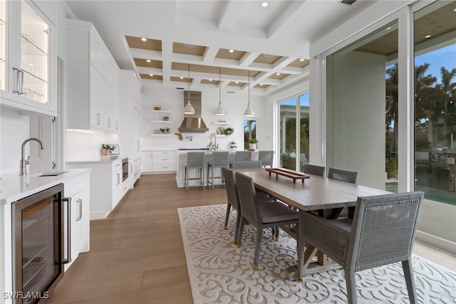 dining area with wine cooler, beam ceiling, coffered ceiling, sink, and light hardwood / wood-style flooring