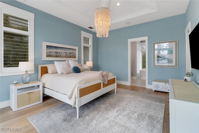 bedroom with a raised ceiling, an inviting chandelier, hardwood / wood-style flooring, and ensuite bathroom