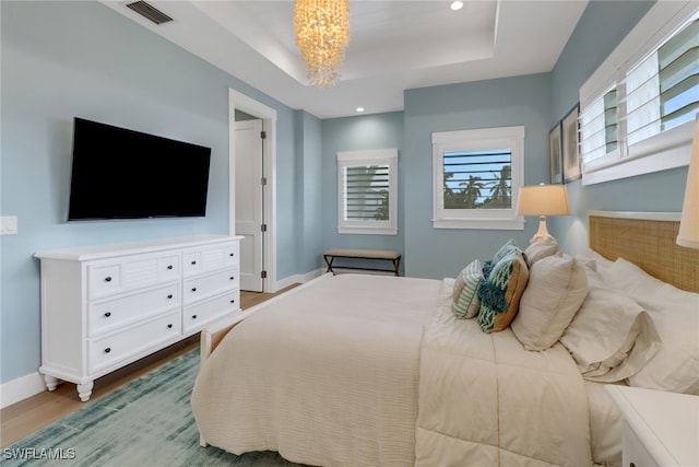 bedroom featuring a chandelier, hardwood / wood-style floors, and a raised ceiling