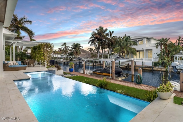 pool at dusk with a dock, a patio, and a water view