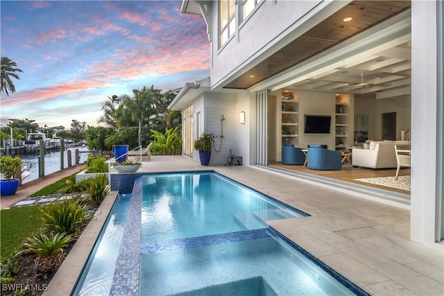 pool at dusk with a dock, a patio, and a water view