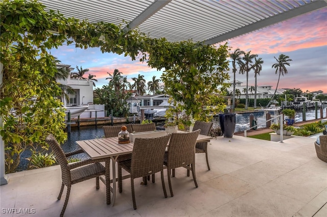 patio terrace at dusk featuring a pergola, a water view, and a boat dock