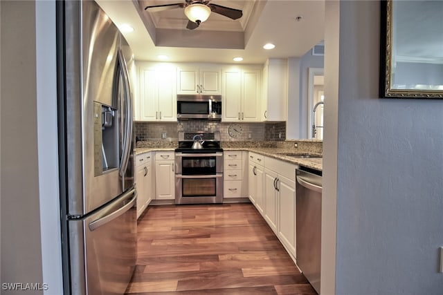 kitchen with a tray ceiling, backsplash, white cabinets, and stainless steel appliances