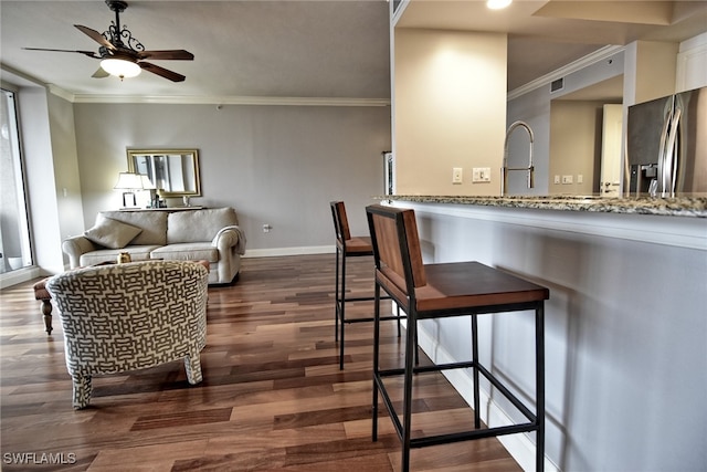 kitchen featuring ceiling fan, dark wood-type flooring, light stone counters, stainless steel fridge, and ornamental molding