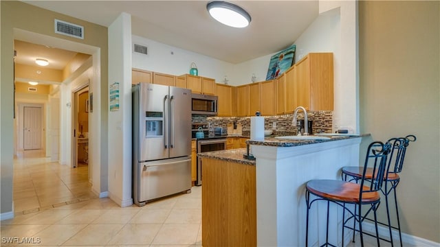 kitchen featuring sink, decorative backsplash, appliances with stainless steel finishes, light tile patterned flooring, and a kitchen bar