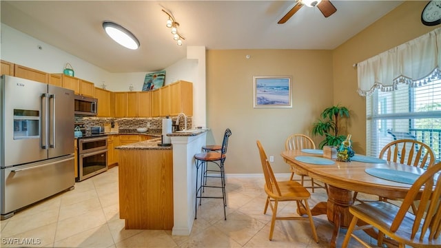 kitchen featuring ceiling fan, a kitchen breakfast bar, kitchen peninsula, decorative backsplash, and appliances with stainless steel finishes