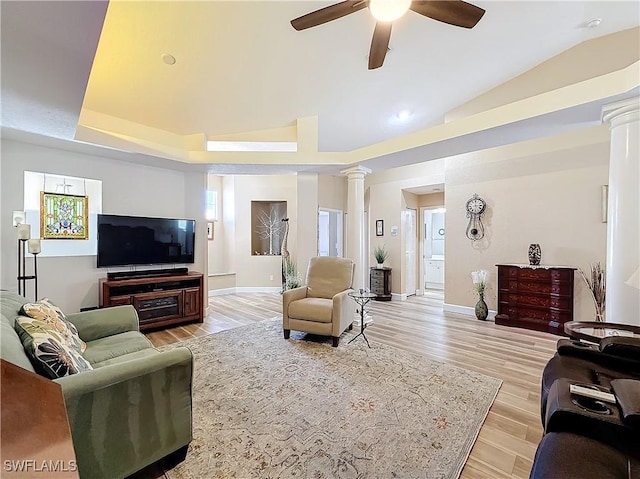 living room featuring ceiling fan, decorative columns, a tray ceiling, vaulted ceiling, and light wood-type flooring