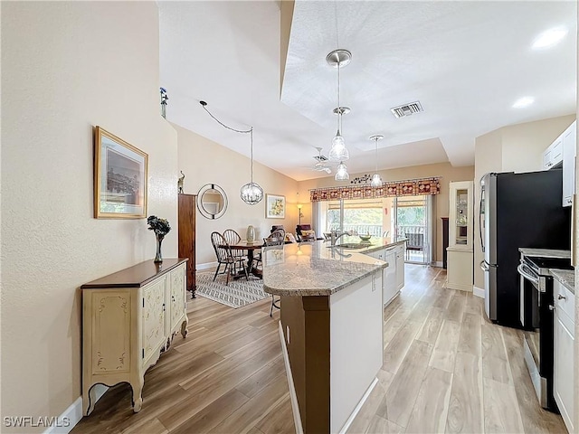 kitchen with decorative light fixtures, white cabinets, a kitchen island with sink, light stone counters, and light hardwood / wood-style flooring