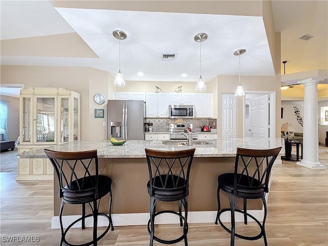 kitchen with stainless steel appliances, a kitchen bar, hanging light fixtures, and ornate columns