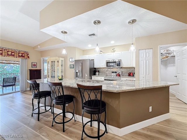 kitchen featuring pendant lighting, stainless steel appliances, light stone countertops, white cabinets, and a large island with sink