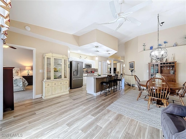 interior space with ceiling fan with notable chandelier, appliances with stainless steel finishes, light hardwood / wood-style floors, a kitchen bar, and decorative light fixtures