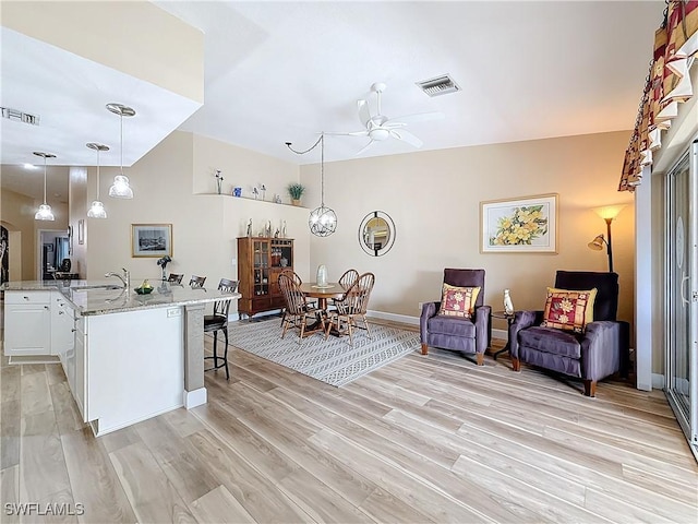 kitchen featuring sink, hanging light fixtures, a kitchen breakfast bar, light stone counters, and white cabinets