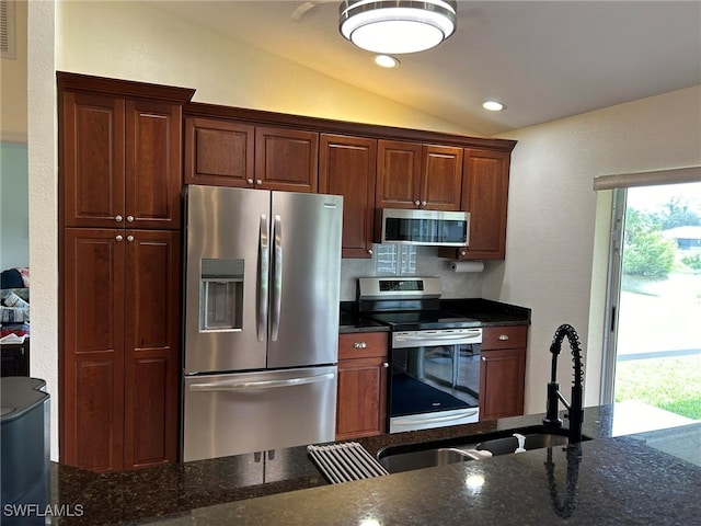 kitchen with vaulted ceiling, appliances with stainless steel finishes, decorative backsplash, and dark stone counters