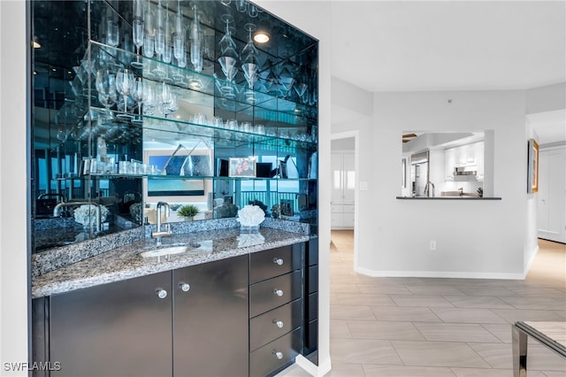 bar with sink, light tile patterned floors, light stone counters, and dark brown cabinetry