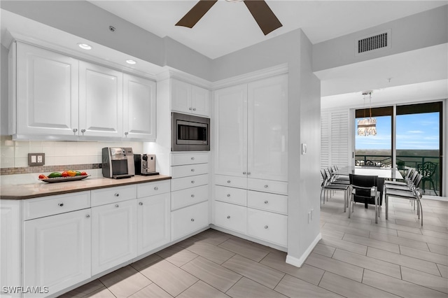 kitchen with white cabinetry, stainless steel microwave, decorative light fixtures, decorative backsplash, and ceiling fan with notable chandelier