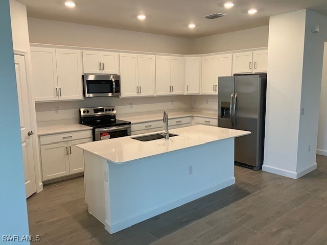 kitchen with appliances with stainless steel finishes, sink, dark hardwood / wood-style flooring, white cabinets, and a center island with sink