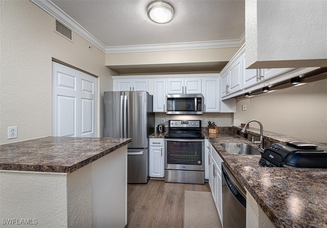 kitchen with hardwood / wood-style floors, white cabinets, crown molding, sink, and stainless steel appliances