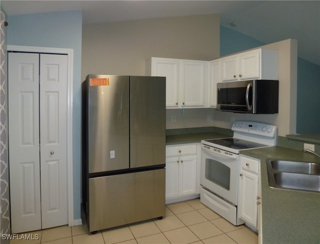 kitchen featuring sink, vaulted ceiling, white cabinets, light tile patterned floors, and appliances with stainless steel finishes