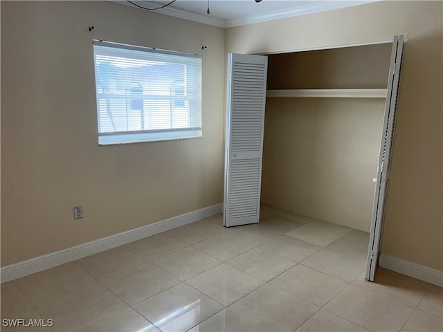 unfurnished bedroom with light tile patterned floors, a closet, and crown molding