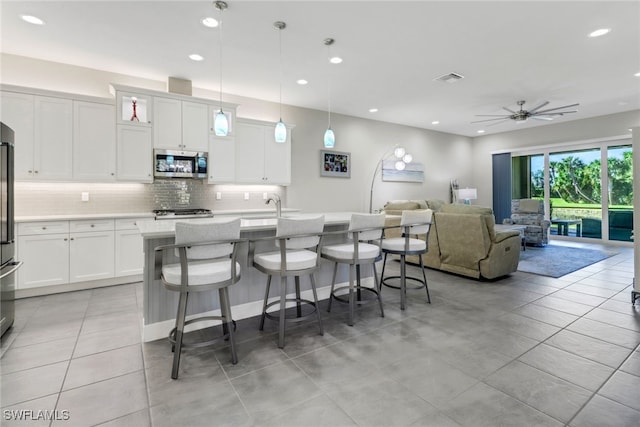 kitchen with stainless steel appliances, a center island with sink, white cabinetry, ceiling fan, and decorative light fixtures