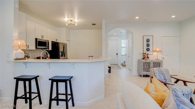 kitchen with light tile patterned floors, a breakfast bar area, white cabinets, black refrigerator with ice dispenser, and kitchen peninsula