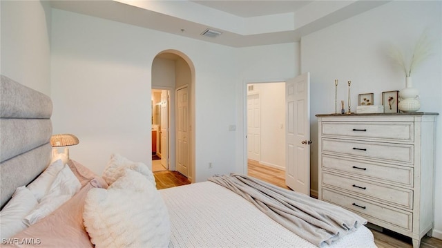 bedroom featuring connected bathroom, light hardwood / wood-style floors, and a raised ceiling