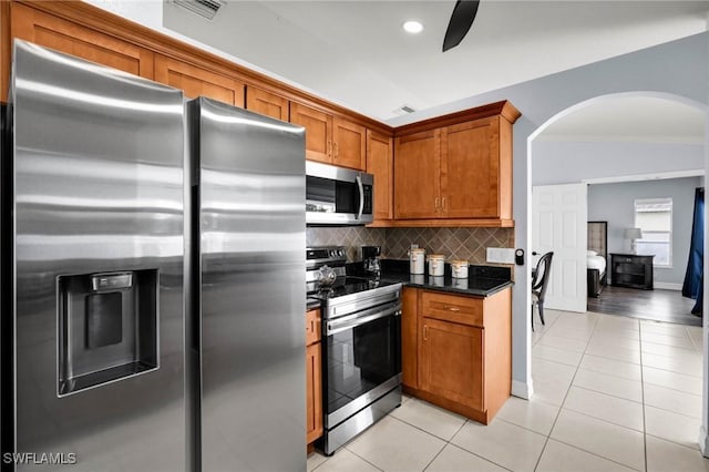 kitchen featuring tasteful backsplash, dark stone countertops, light tile patterned floors, and stainless steel appliances