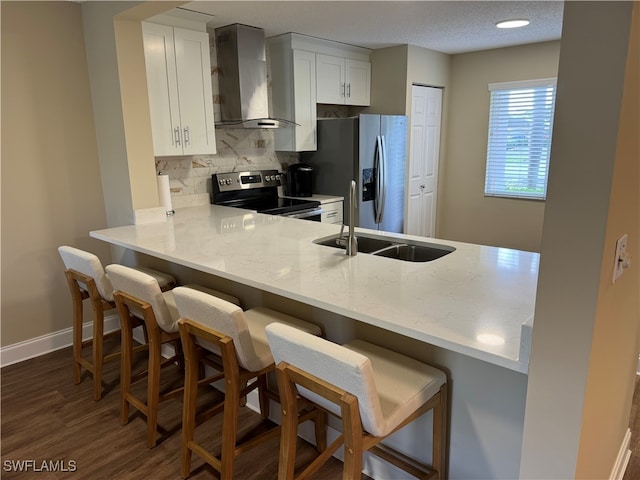 kitchen featuring wall chimney exhaust hood, a breakfast bar area, sink, white cabinetry, and appliances with stainless steel finishes