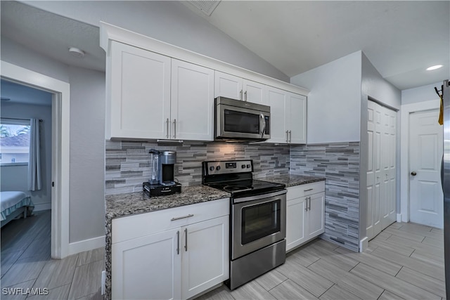 kitchen with stainless steel appliances, white cabinetry, and dark stone countertops