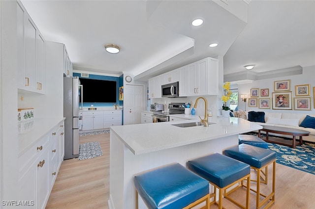 kitchen with appliances with stainless steel finishes, white cabinetry, sink, a kitchen bar, and kitchen peninsula