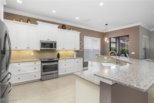 kitchen with stainless steel appliances, a center island with sink, sink, white cabinetry, and decorative light fixtures