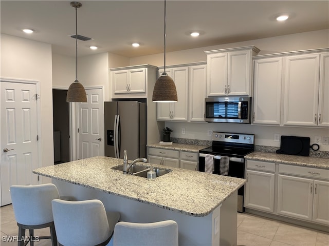 kitchen featuring a center island with sink, stainless steel appliances, light stone countertops, pendant lighting, and sink