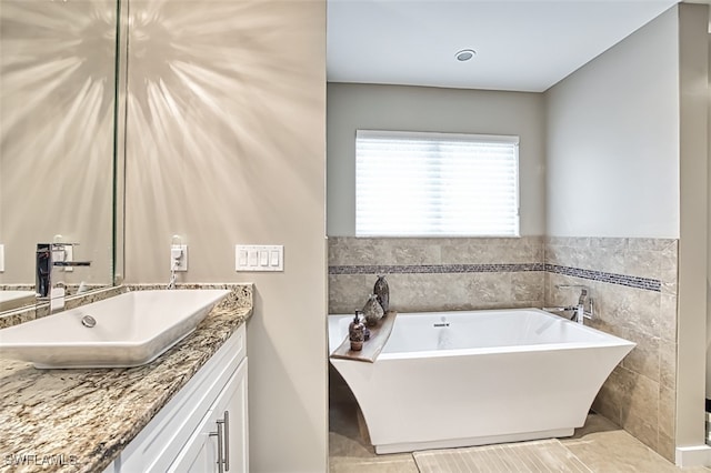 bathroom with tile walls, a tub to relax in, vanity, and tile patterned floors