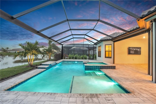 pool at dusk with an in ground hot tub, a water view, and glass enclosure