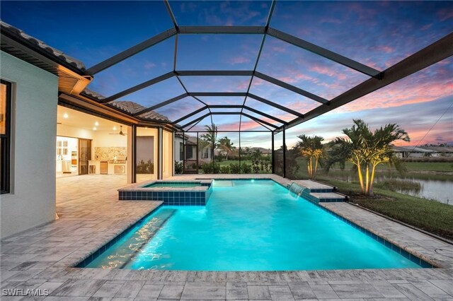 pool at dusk with glass enclosure, a water view, pool water feature, an in ground hot tub, and a patio