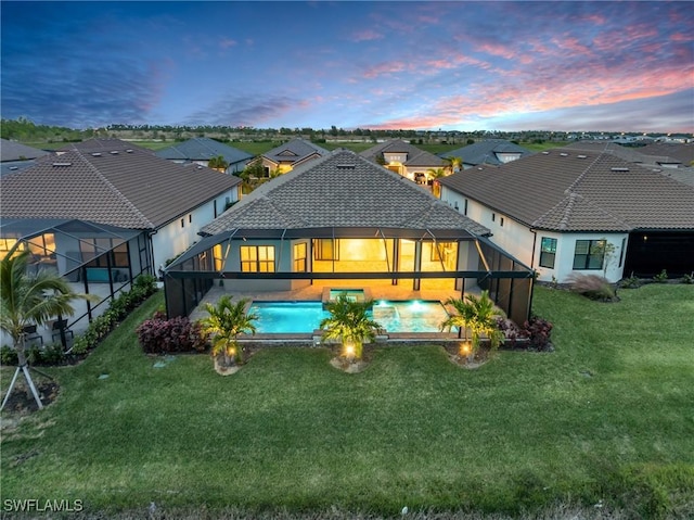 back of house at dusk featuring an outdoor pool, a lanai, a yard, and a tiled roof