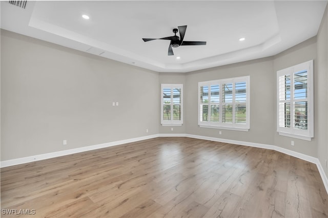 spare room with a raised ceiling, ceiling fan, and light wood-type flooring