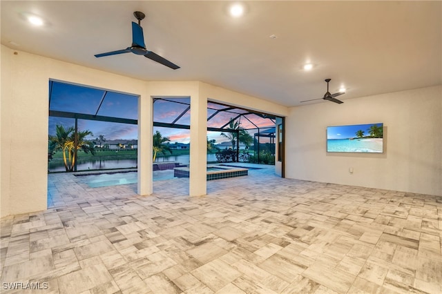 patio terrace at dusk featuring a water view, ceiling fan, a lanai, and a pool with hot tub