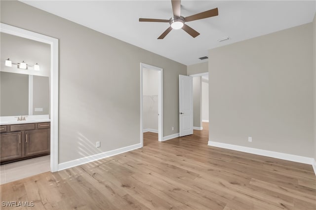 unfurnished bedroom with sink, ensuite bathroom, a walk in closet, a closet, and light wood-type flooring