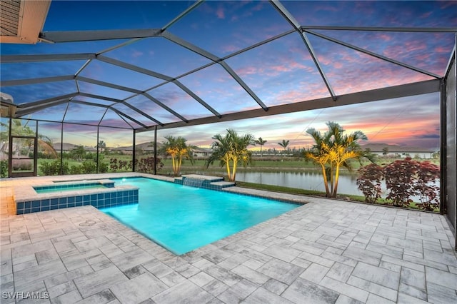 pool at dusk featuring an in ground hot tub, a water view, glass enclosure, and a patio area