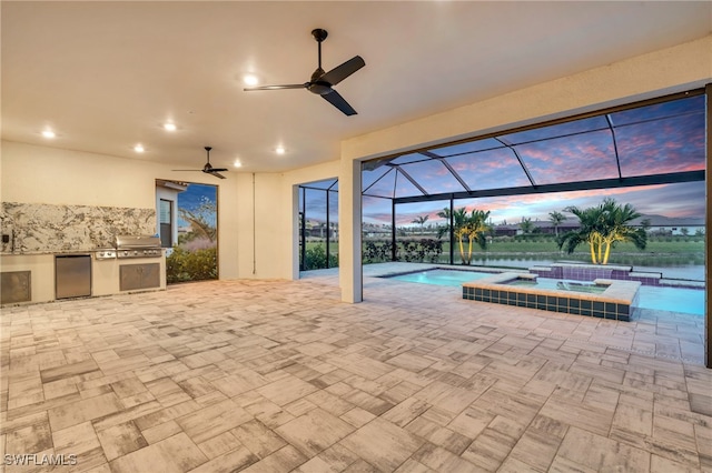 patio terrace at dusk featuring glass enclosure, an outdoor kitchen, a water view, a pool with hot tub, and ceiling fan