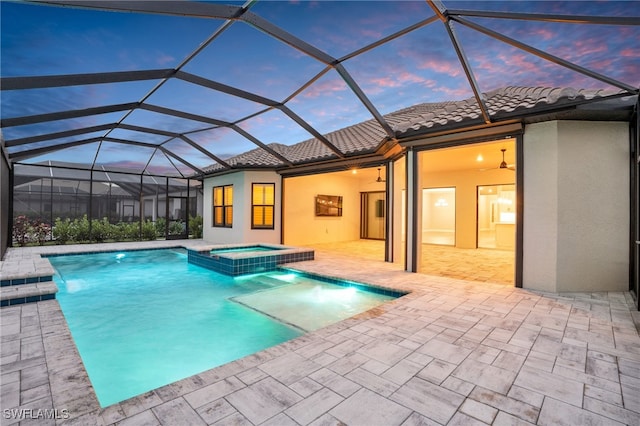 pool at dusk featuring an in ground hot tub, pool water feature, a patio, and glass enclosure