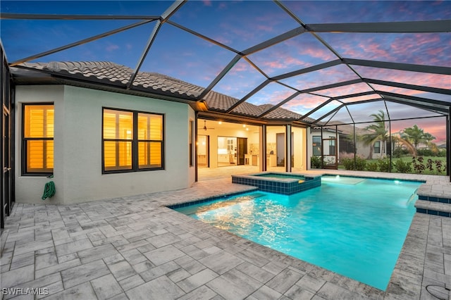 pool at dusk featuring glass enclosure, ceiling fan, a patio area, and an in ground hot tub