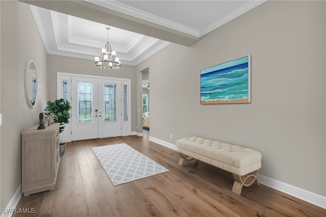 entryway featuring french doors, a notable chandelier, light wood-type flooring, a tray ceiling, and ornamental molding