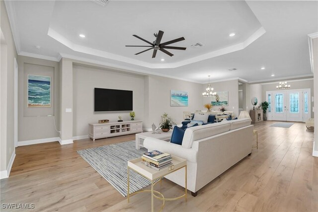 living room with french doors, light hardwood / wood-style floors, crown molding, and a tray ceiling