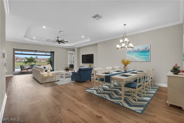 dining area with light wood-type flooring, a tray ceiling, and ornamental molding