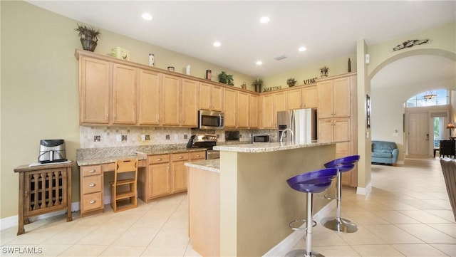 kitchen with light stone countertops, appliances with stainless steel finishes, decorative backsplash, a center island with sink, and a breakfast bar area